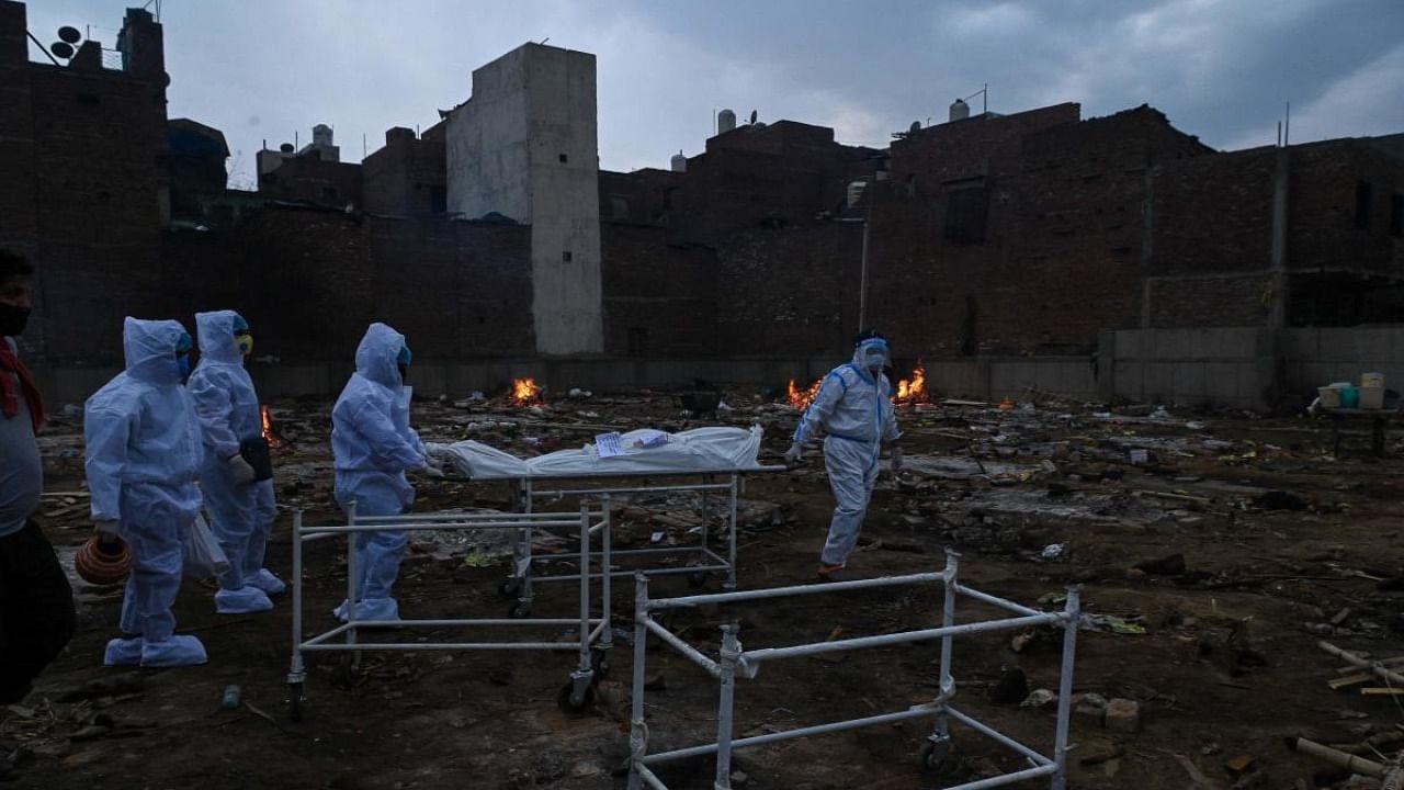 Relatives in personal protective equipment (PPE) suits carry the body of a person who died due to the Covid-19 coronavirus, at a cremation ground in New Delhi. Credit: AFP Photo