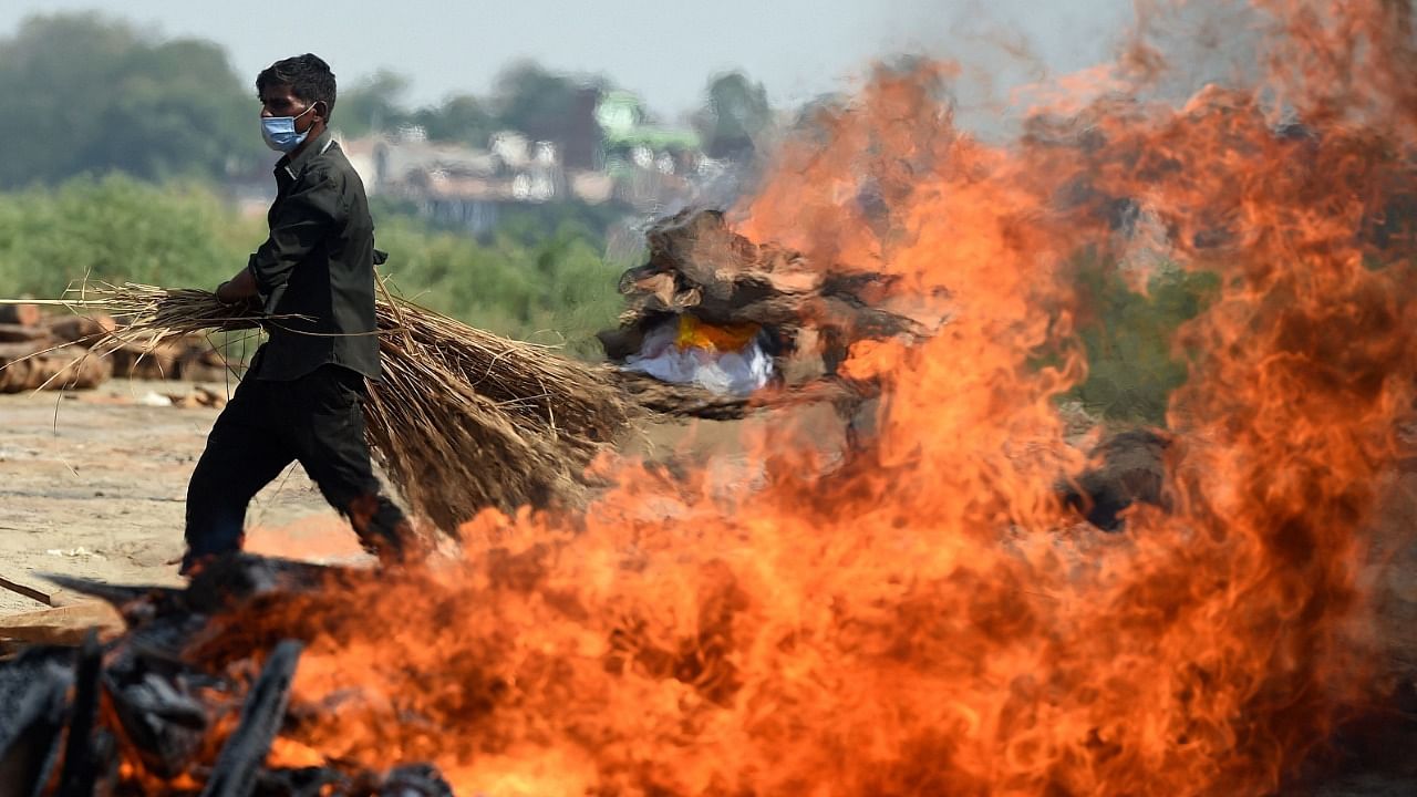 A worker walks past a burning funeral pyre of a person who died due to the Covid-19 coronavirus at a cremation ground in Allahabad on May 8, 2021. Credit: AFP Photo