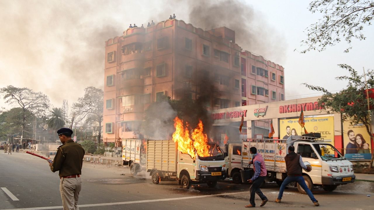 A policeman stands near a burning vehicle, set ablaze allegedly by an irrate mob, near BJP party office in Burdwan district. Credit: PTI File Photo