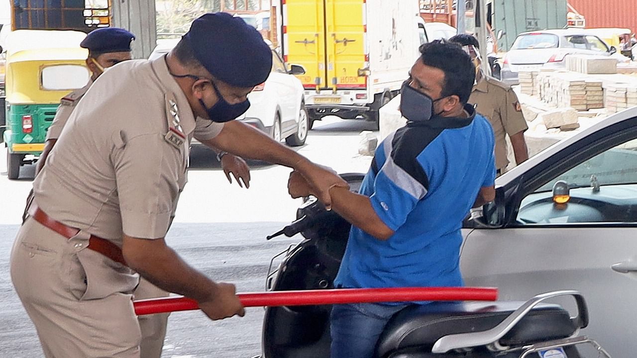 A police man punishes a scooterist for flouting Covid-19 lockdown rules, in Bengaluru, Saturday, May 8, 2021. Credit: PTI Photo