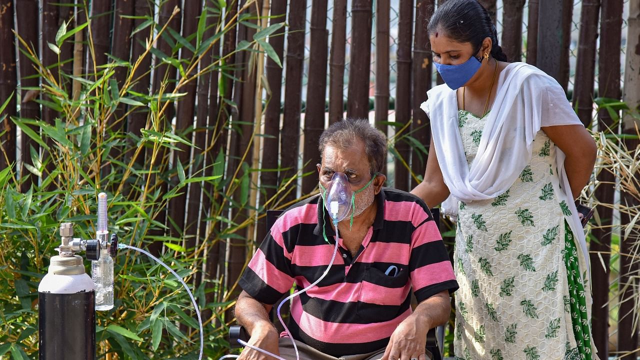 A family member of a Covid-19 patient assists him to breathe at an oxygen dispensing centre in Bengaluru, Saturday, May 8, 2021. Credit: PTI Photo