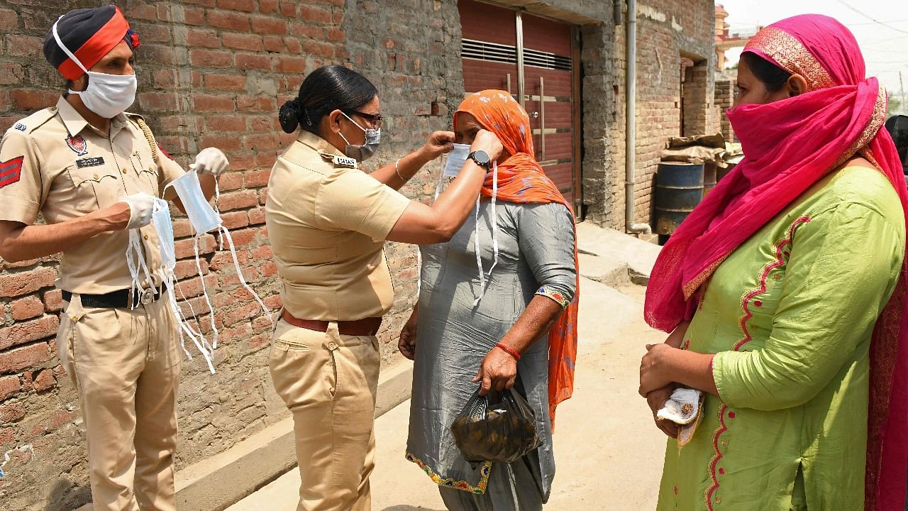 A police officer ties a facemask on a woman after police in rural areas launched a free cab service for villagers to the Covid-19 coronavirus testing and vaccination centres on the outskirts of Amritsar. Credit: AFP Photo