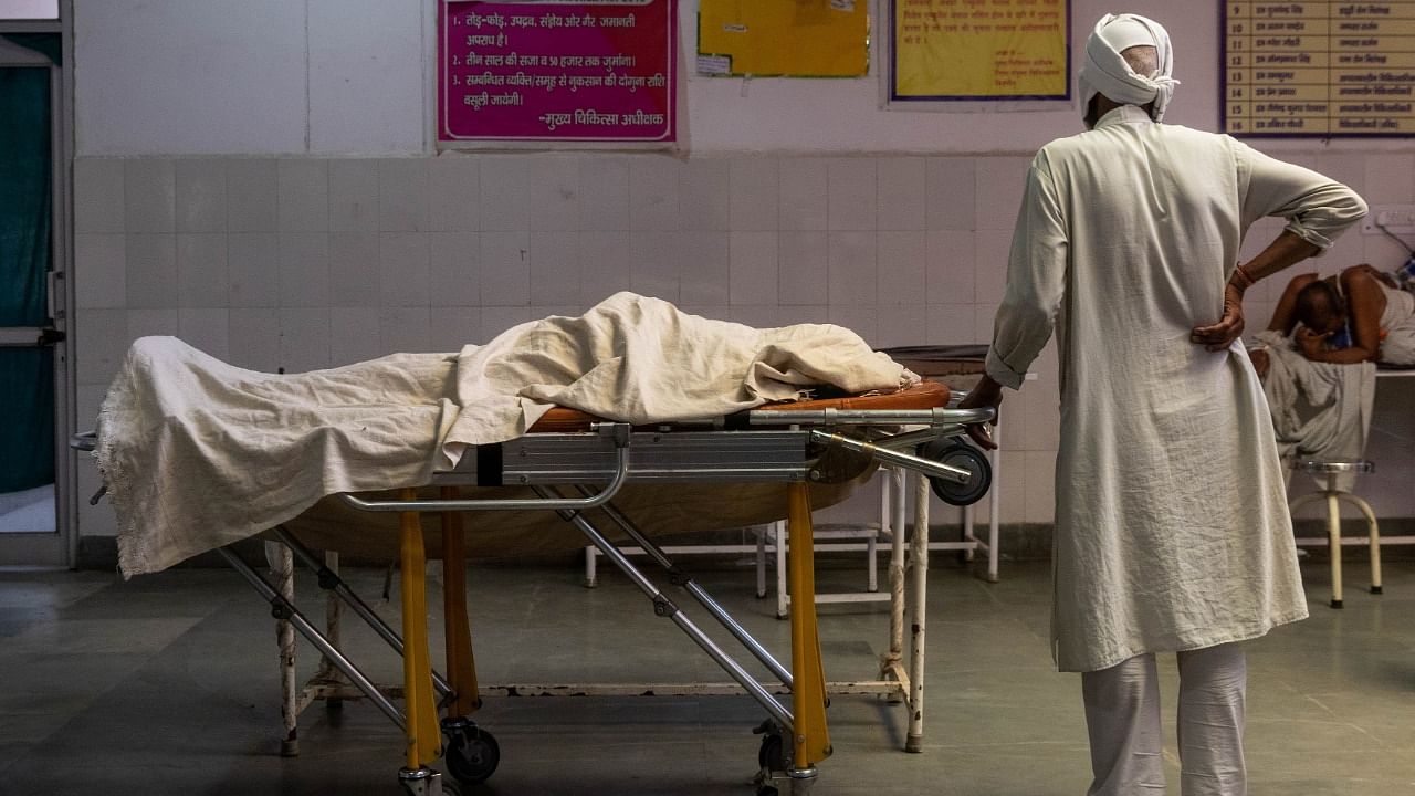 A man stands next to the body of his wife, who died due to breathing difficulties, inside an emergency ward of a government-run hospital, amidst the coronavirus pandemic, in Bijnor, Uttar Pradesh, India, May 11, 2021. Credit: Reuters Photo