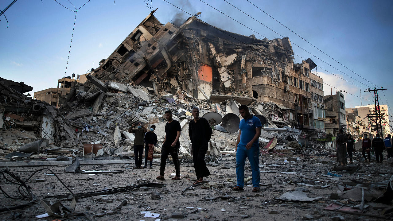 Palestinians walk next to the remains of a destroyed 15-storey building after being hit by Israeli airstrikes on Gaza City. Credit: AP Photo