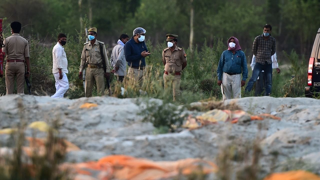 Police and administrative officials (background) inspect a cremation ground on the banks of Ganges River, where suspected bodies (foreground) of Covid-19 coronavirus victims appeared partially buried, at Rautapur Ganga Ghat in Unnao on May 13, 2021. Credit: AFP Photo