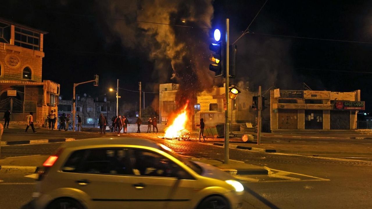 A car drives past a burning barricade set up by Palestinian protesters in the Shuafat Palestinian neighbourhood, near the Israeli settlement of Ramat Shlomo, in Israeli-annexed east Jerusalem. Credit: AFP Photo