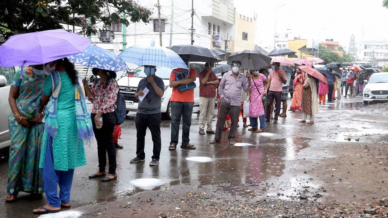 Beneficiaries wait in a queue to receive Covid-19 vaccine dose during in rain at a vaccination centre in in Coimbatore. Credit: PTI Photo