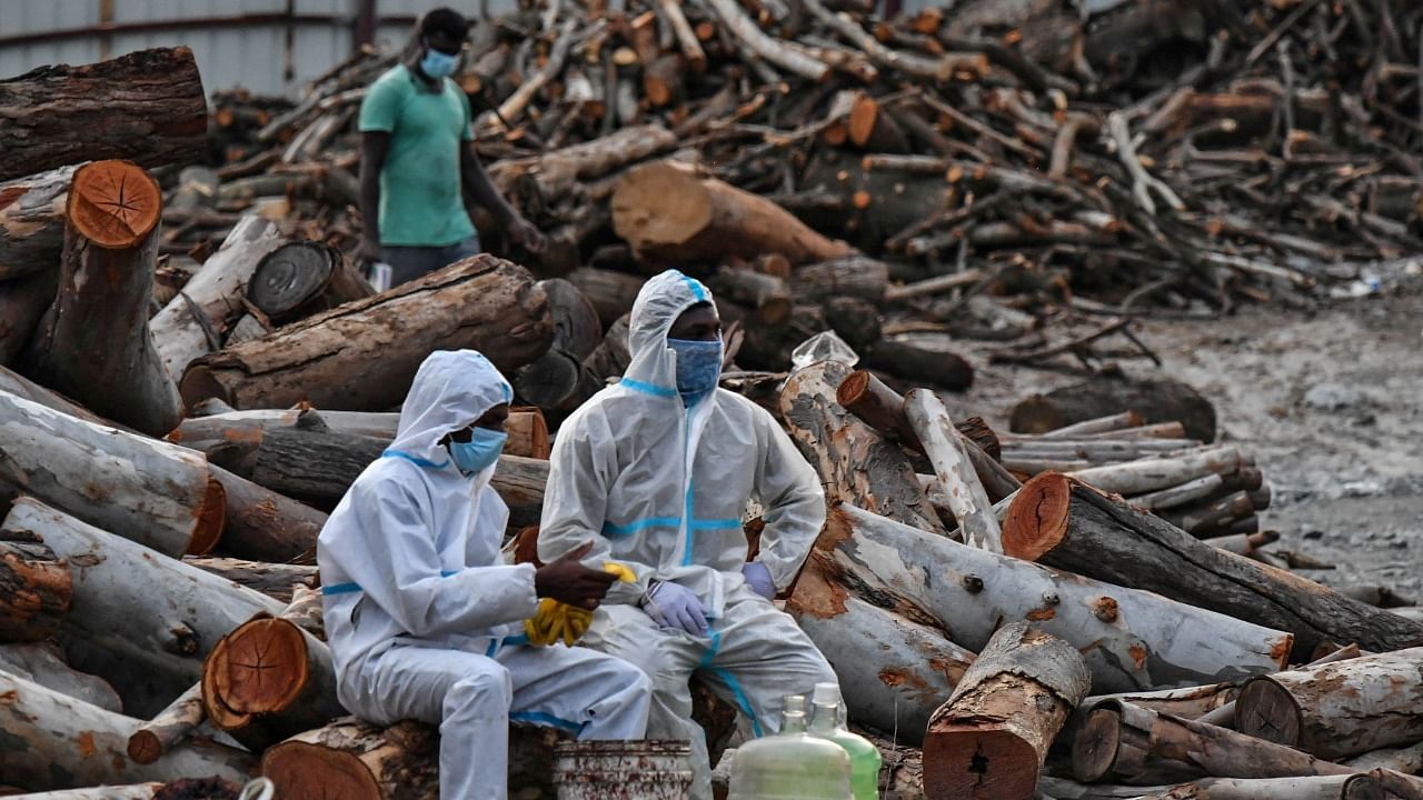 Volunteers take a break during the cremation of people who died due to the coronavirus, at a crematorium ground. Credit: Reuters Photo