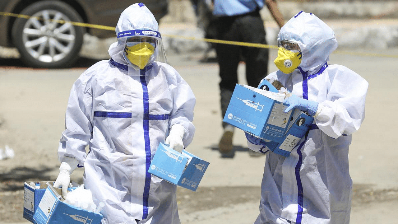 Healthcare workers wearing PPE kits carry syringes towards a Covid-19 vaccination centre in Jammu. Credit: PTI Photo
