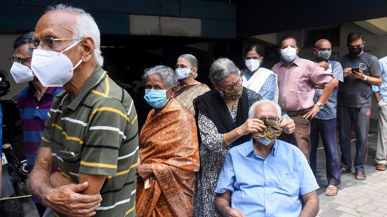 A woman puts a mask to her husband while waiting for vaccination against Covid-19, in Kochi, Saturday, May 8, 2021. Credit: PTI Photo