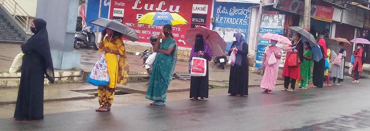 Women wait in a queue, amid the rain, in front of a fair price shop in Gonikoppa.