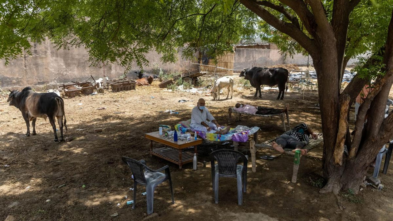 A villager suffering from Covid-19 sits in a cot as he receives treatment at a makeshift open-air clinic, amidst the spread of the coronavirus disease, in Mewla Gopalgarh village, in Jewar district. Credit: Reuters Photo