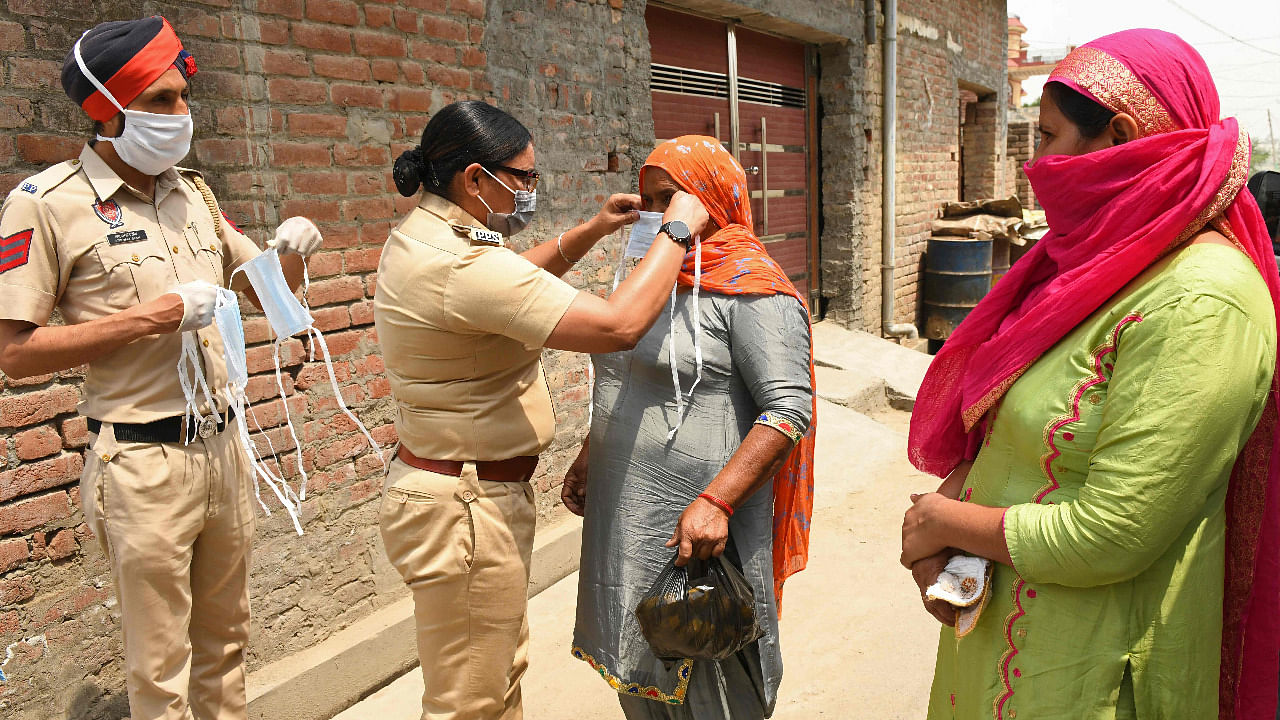 A police officer ties a facemask on a woman after police in rural areas launched a free cab service for villagers to the Covid-19 testing and vaccination centres on the outskirts of Amritsar. Credit: AFP Photo