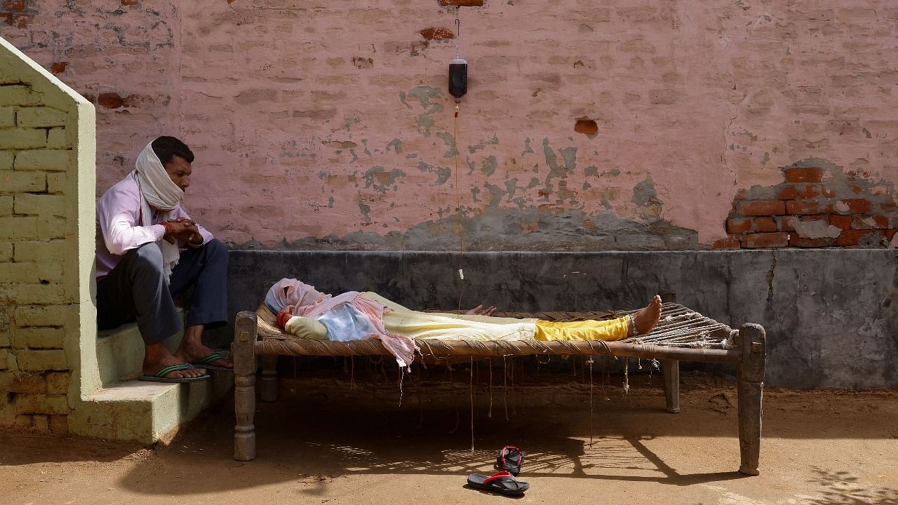 A man sits next to his wife, who is suffering from fever as she receives treatment at a clinic set up by a local villager, amidst the spread of the coronavirus disease (Covid-19), in Parsaul village in Greater Noida. Credit: Reuters Photo
