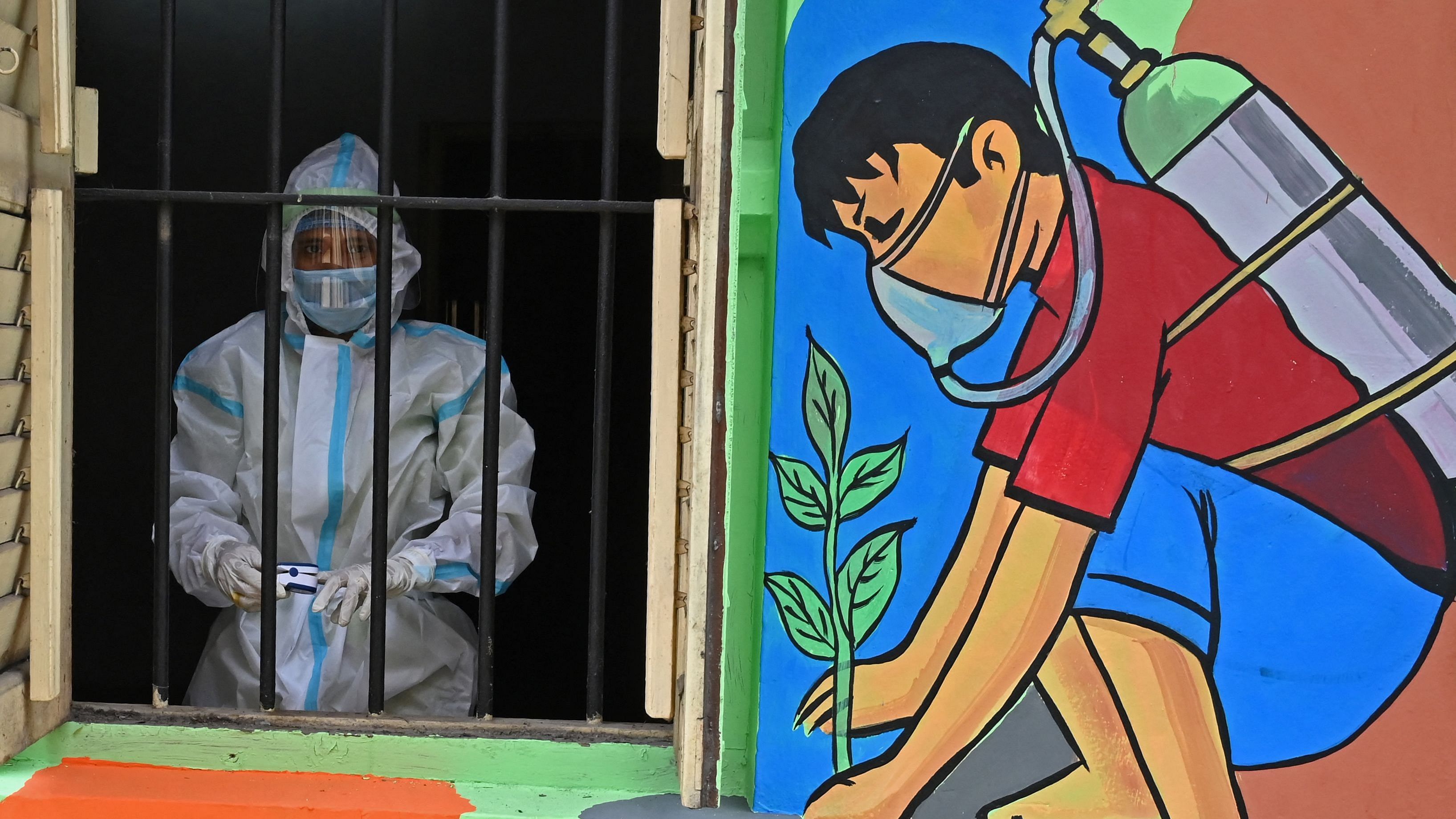 A health worker wearing a protective suit stands on the window of a newly inaugurated 'Oxygen Hub' for Covid-19 coronavirus patients in Kolkata. Credit: AFP File Photo