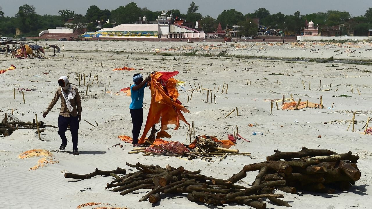 Workers remove saffron cloths of dead bodies buried in the sand near a cremation ground on the banks of the Ganges River in Shringaverpur village, around 40 km from Allahabad on May 24, 2021. Credit: AFP Photo