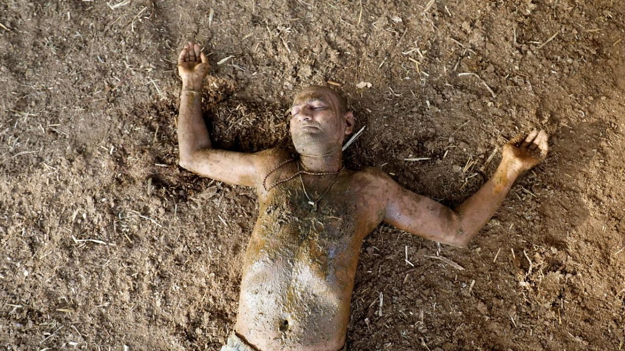 Man lies on the ground after applying cow dung on his body during "cow dung therapy", believing it will boost his immunity against the coronavirus. Credit: Reuters Photo