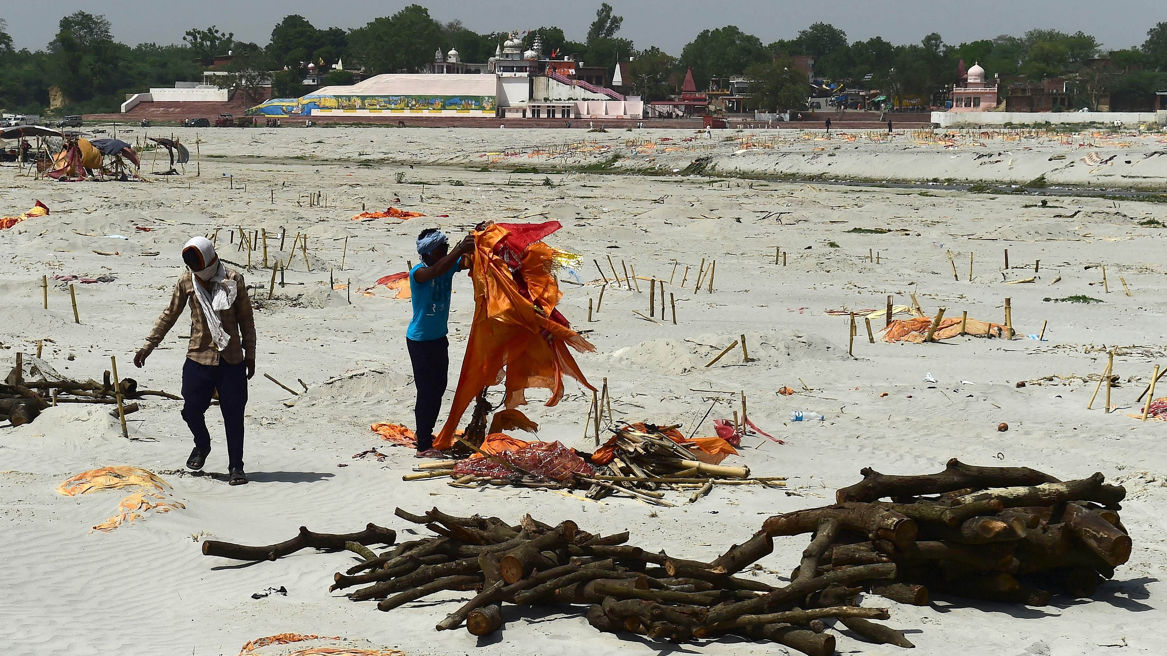 Workers remove saffron cloths of dead bodies buried in the sand near a cremation ground on the banks of the Ganga. Credit: AFP Photo