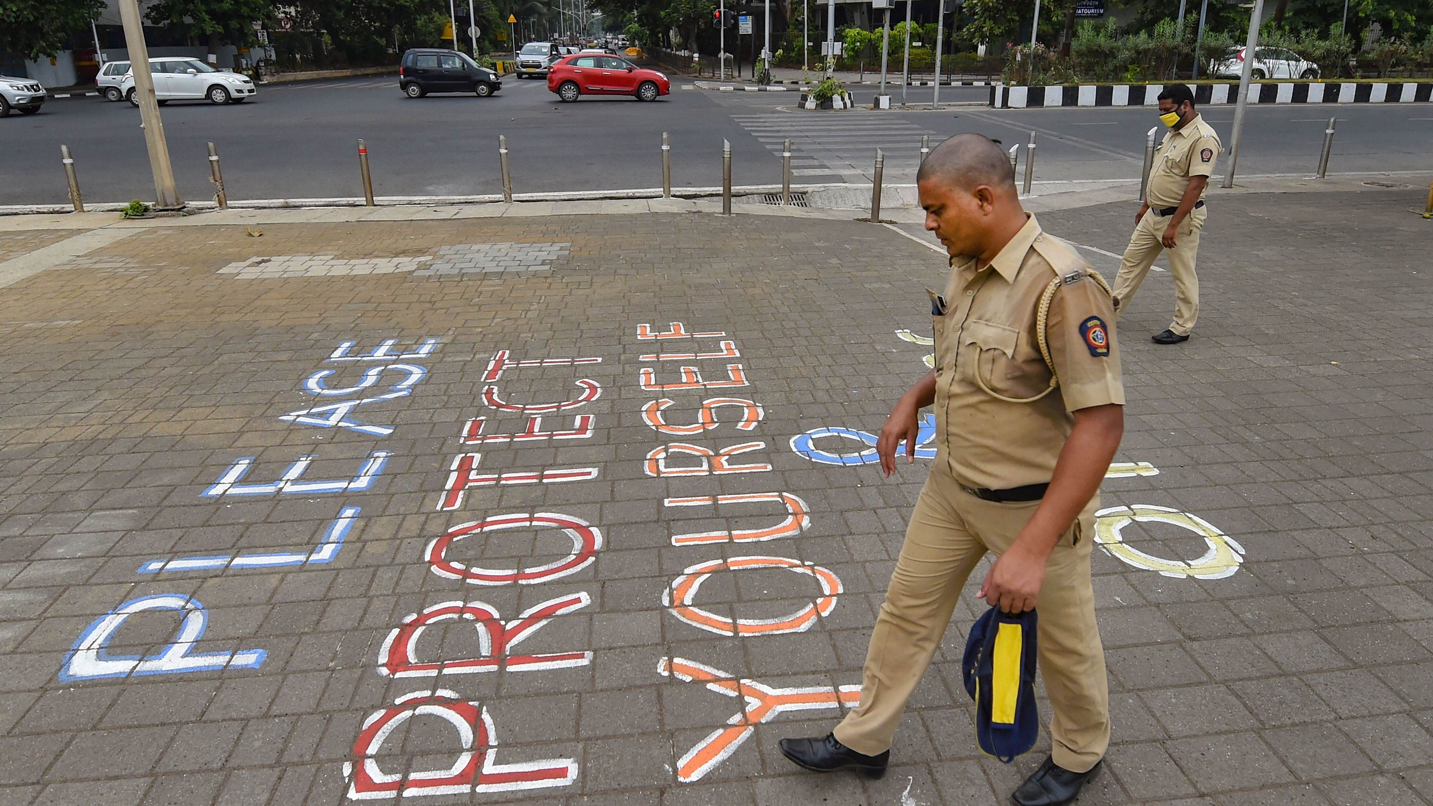 Police personnel walk past a painted message that reads 'Please Protect Yourself And Others' at Marine Drive promenade. Credit: PTI File Photo