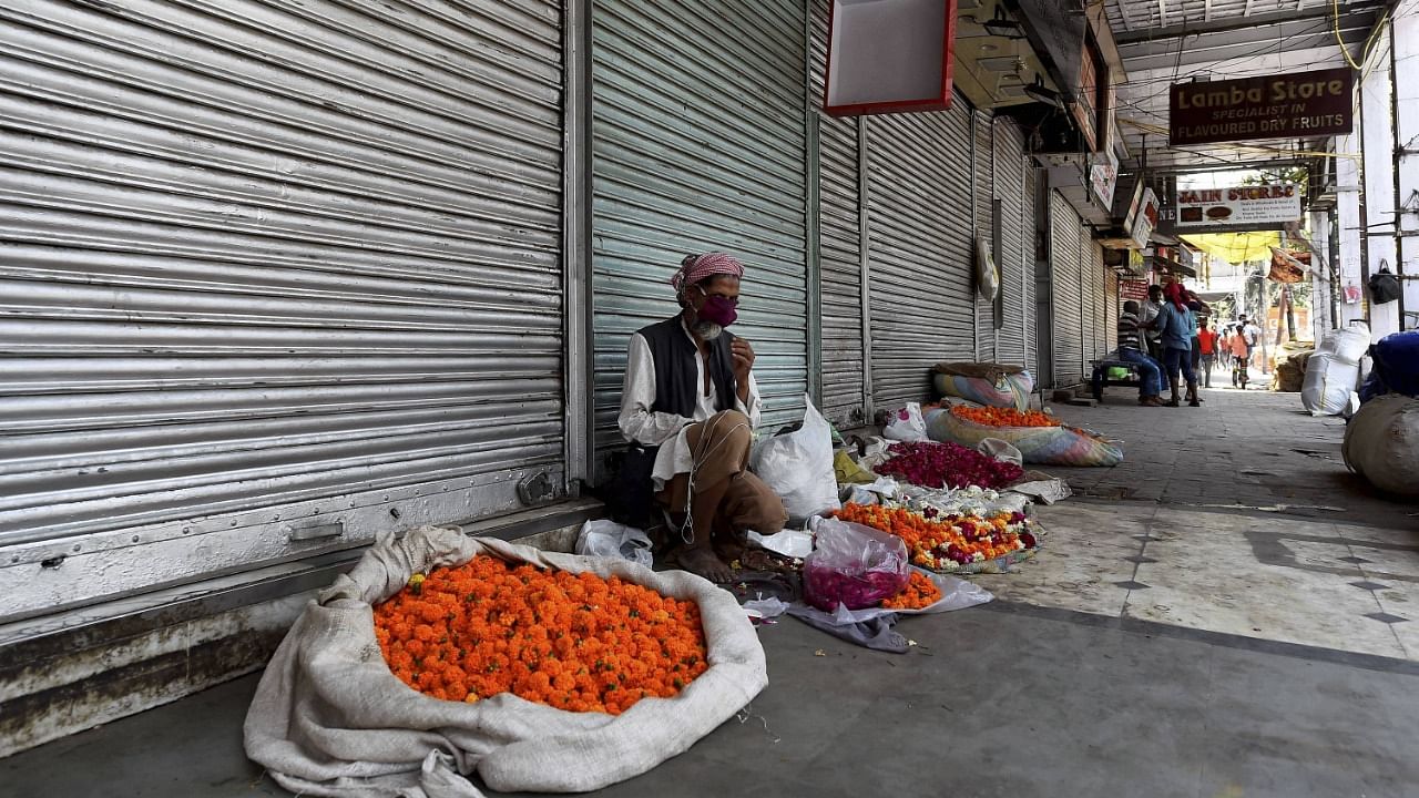 A man sells flowers outside a closed shop during Covid-induced lockdown, at Khari Baoli market in New Delhi. Credit: PTI File Photo