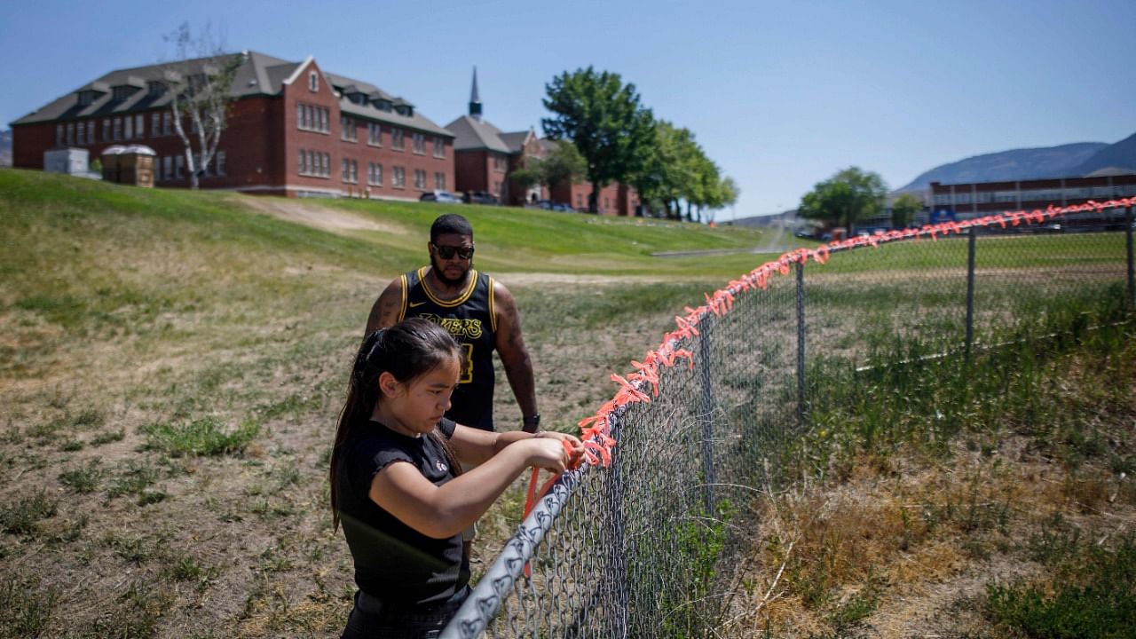 Autumn Peters places 215 ribbons on the fence behind the former Kamloops Indian Residential School, in honor of the 215 children whose remains have been discovered buried near the facility. Credit: AFP Photo