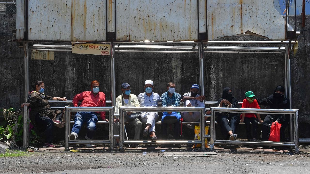 Commuters wearing facemasks as a protective measure against the spread of the Covid-19 coronavirus wait for their transport at bus stop, in Mumbai. Credit: AFP Photo