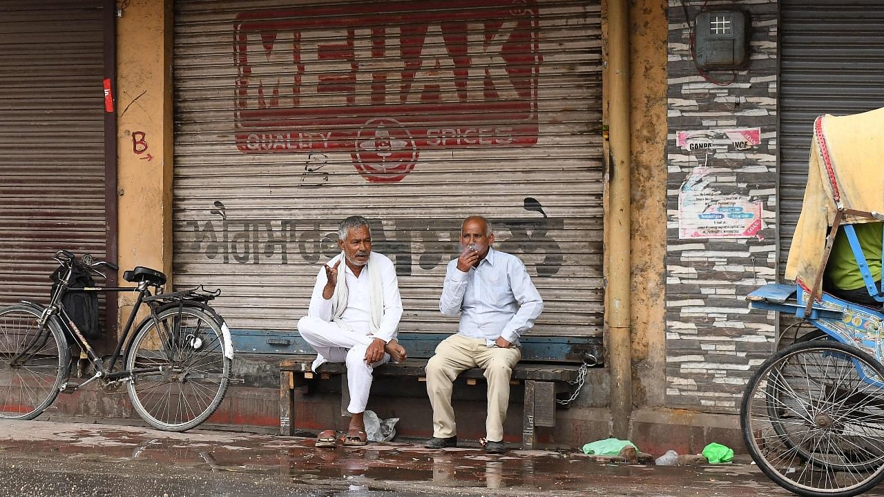 People sit outside a closed shop during weekend lockdown in Amritsar. Credit: AFP Photo