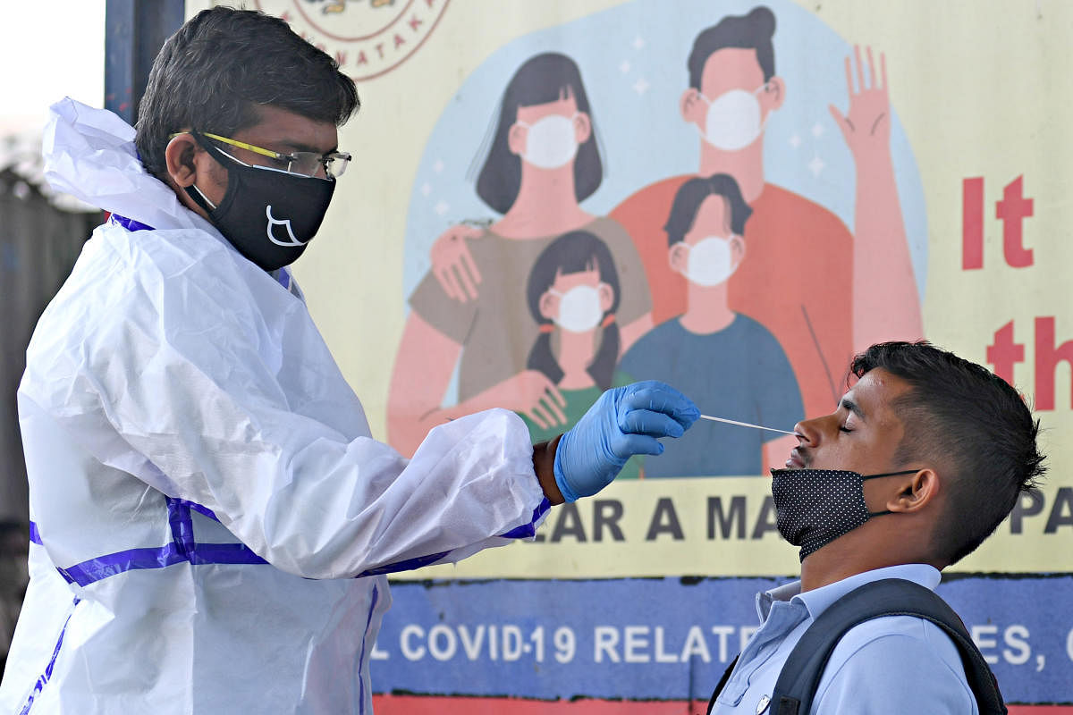 A health care worker collects a swab sample from a man for the coronavirus near KR Market in Bengaluru. Credit: DH Photo