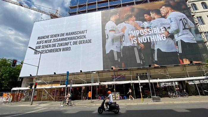 A person rides a scooter past a building under construction covered in a massive billboard with an advertisement featuring the German national football team ahead of the upcoming UEFA Euro 2020 football championships in Berlin's Kreuzberg district on June 6, 2021. Credit: AFP Photo