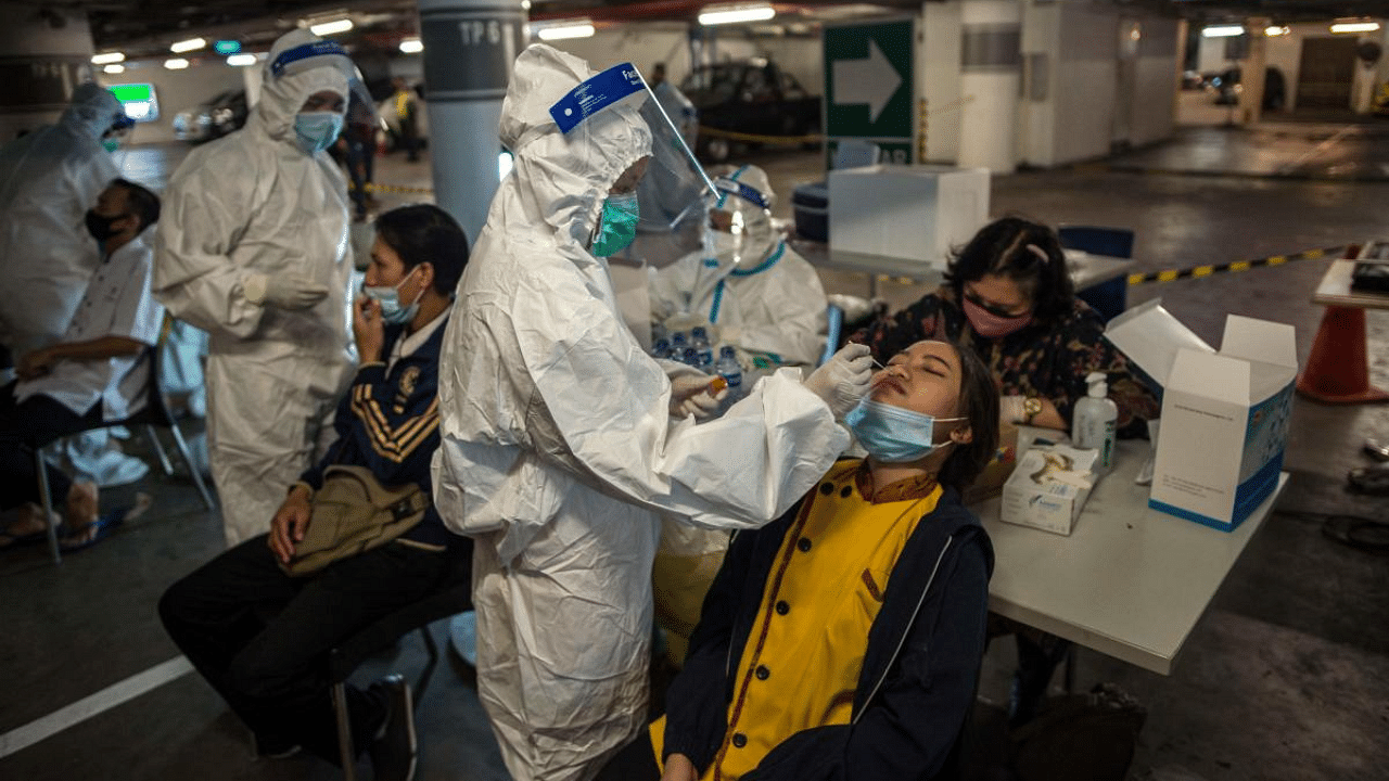 Health workers collect swab samples from shoppers to test for the Covid-19 before they are allowed to enter a shopping mall in Surabaya. Credit: AFP Photo