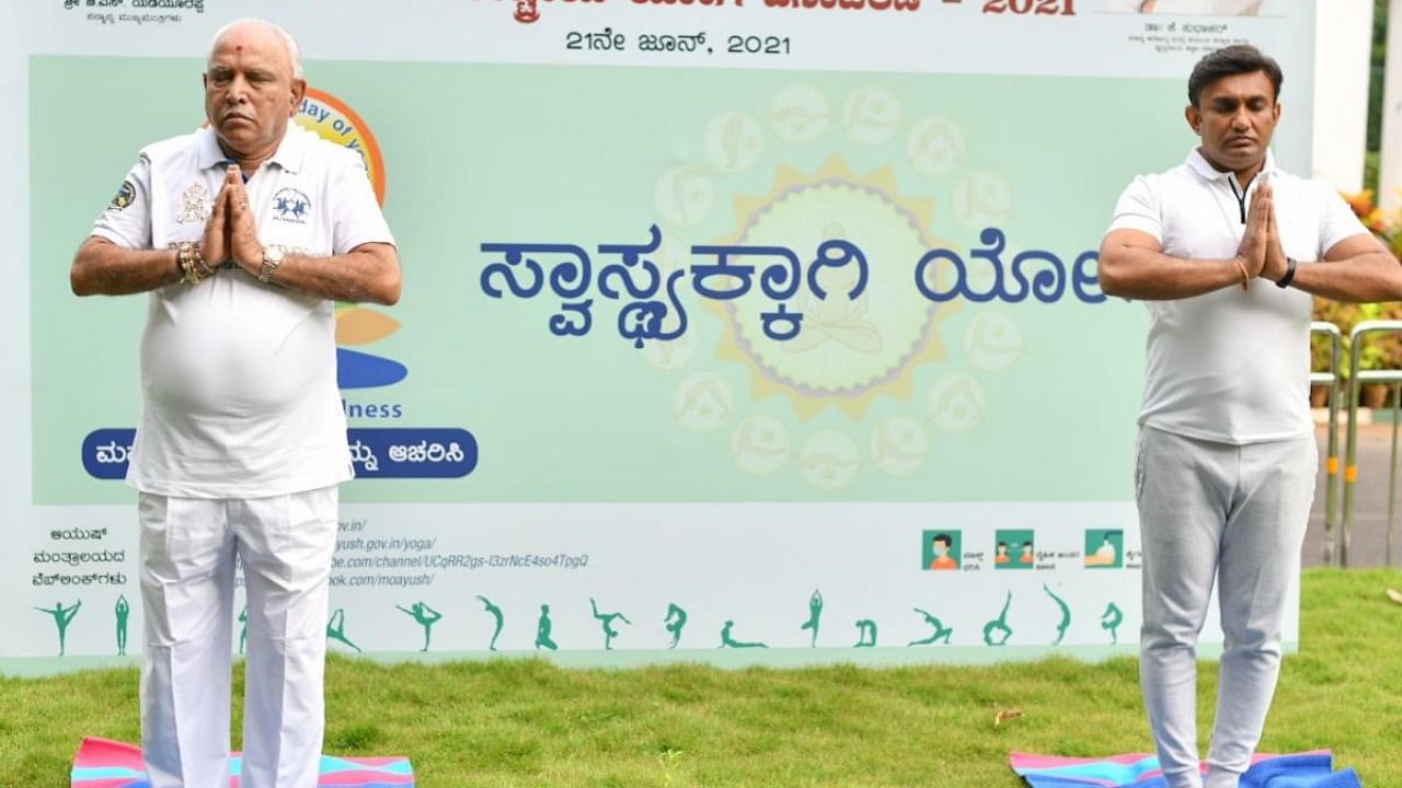 Chief Minister B S Yediyurappa and Health and Medical Education Minister Dr K Sudhakar perform yoga on the occasion of International Day of Yoga, in Bengaluru on Monday. Credit: Information Department