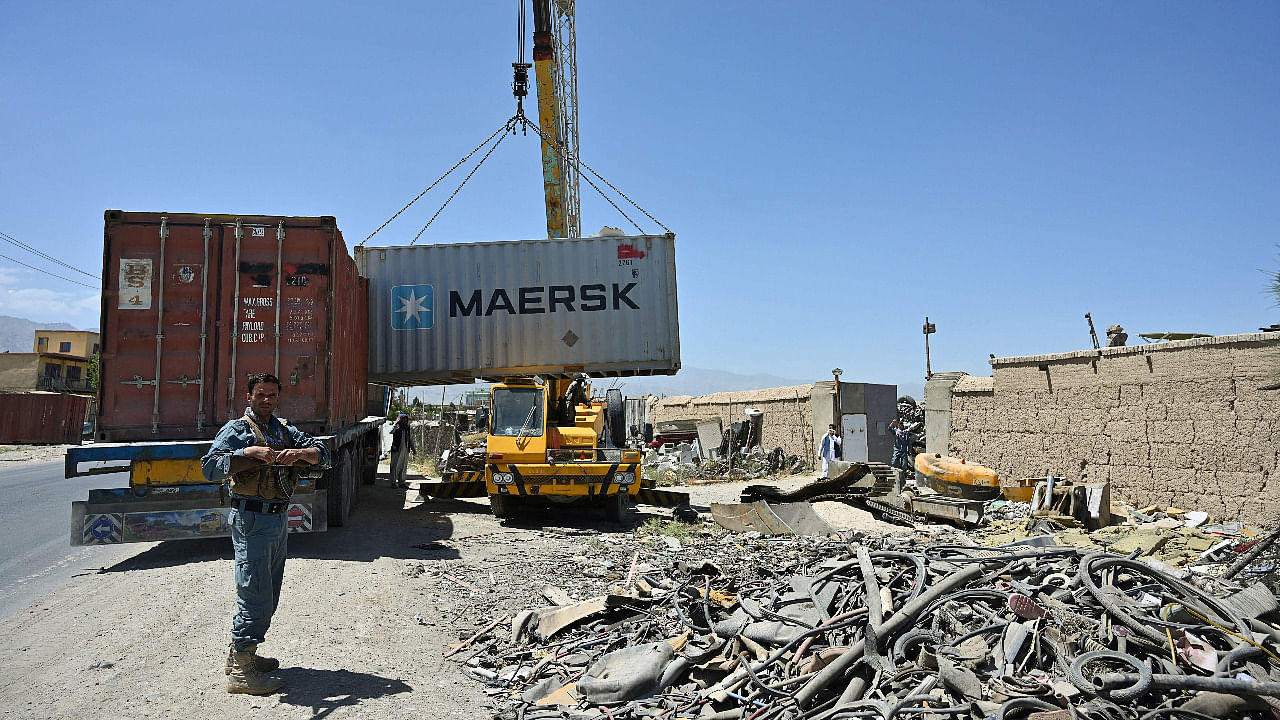 Policemen stand guard as workers unload a container at a junkyard near the Bagram Air Base in Bagram. Credit: AFP Photo