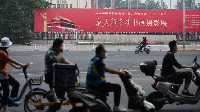 In this photo taken on June 9, 2021, people ride past a propaganda slogan which reads "Forever Follow the Party", outside an exhibition of calligraphy, painting and photography celebrating the 100th anniversary of the founding of the Communist Party, at an exhibition centre in Beijing. Credit: AFP Photo