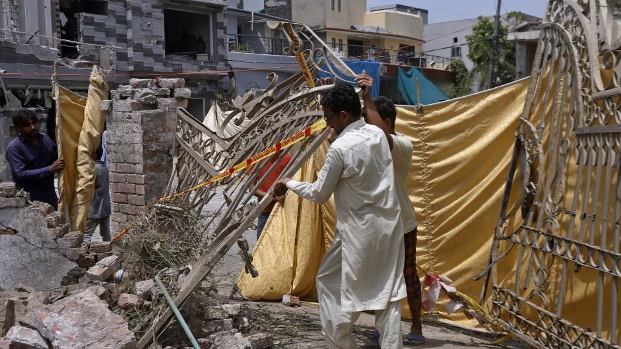 Residents remove a gate from their damaged house at the site of a car bombing Wednesday, in Lahore, Pakistan, Thursday, June 24, 2021. Credit: AP Photo