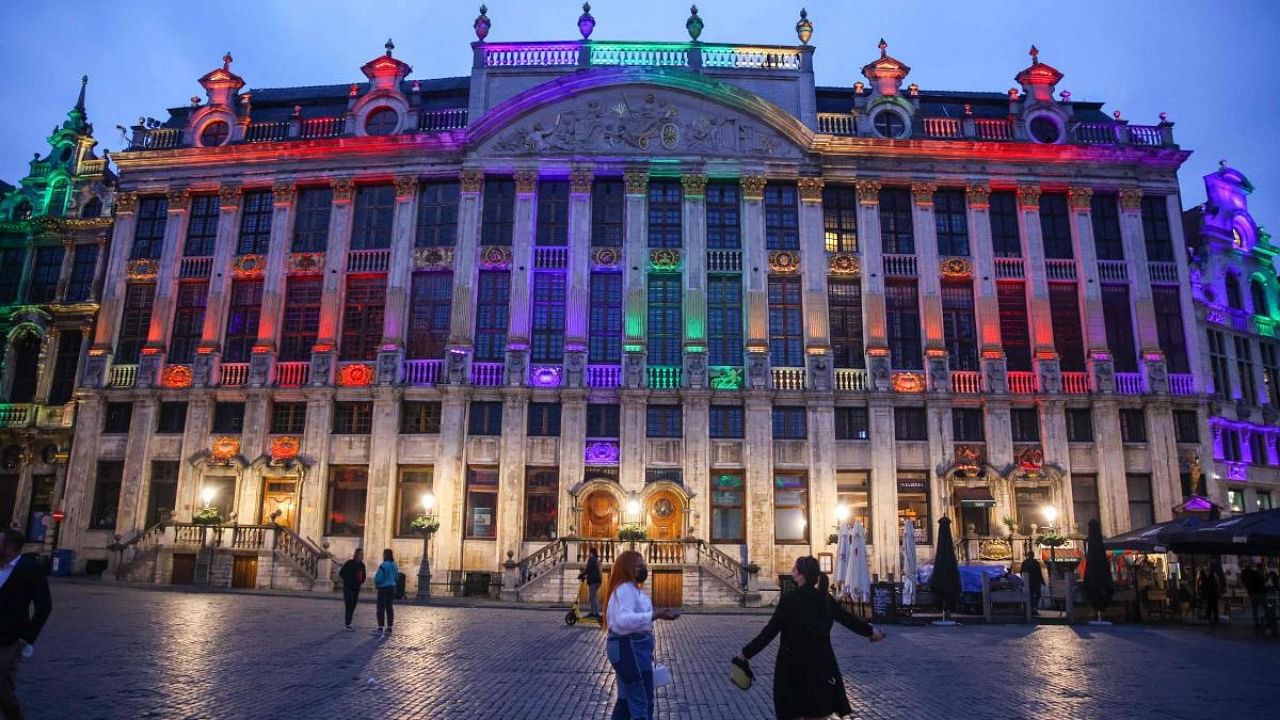 Passers-by stand in front of the Brussels Town Hall and the rest of the historical Grand Place in Brussels lit with the rainbow colours to show solidarity to the LGTBQ+ community after the anti-gay vote in Hungary and the position of UEFA in Brussels, on June 23, 2021. Credit: AFP Photo