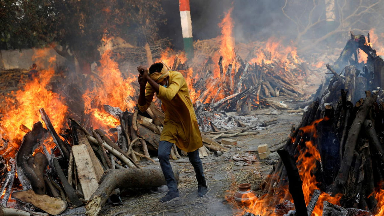 A man runs past the burning funeral pyres of those who died from the coronavirus disease during a mass cremation, at a crematorium in New Delhi. Credit: Reuters Photo