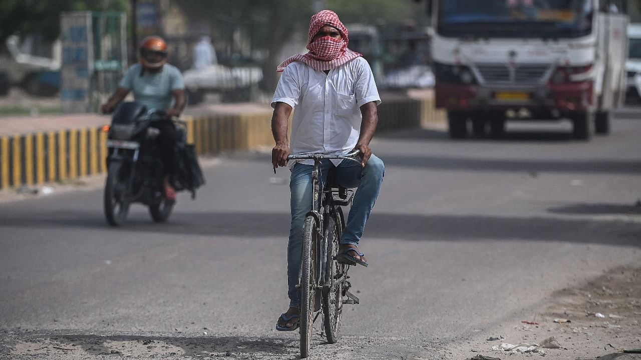 A cyclist covers his face with a cloth to shield from the scorching sun as he peddles along a road on a hot summer afternoon in Rajasthan. Credit: AFP Photo