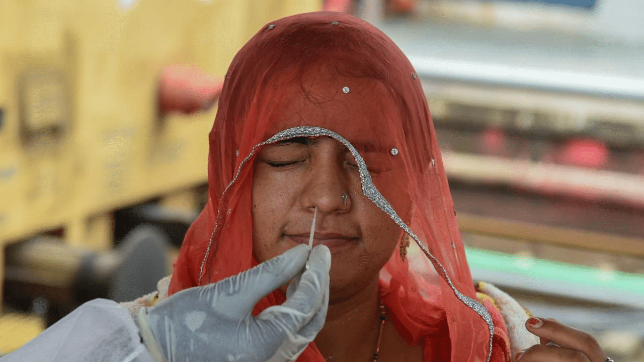 A health worker takes a nasal swab sample of a passenger for the Covid-19 test after arriving at a railway platform in Mumbai. Credit: AFP Photo