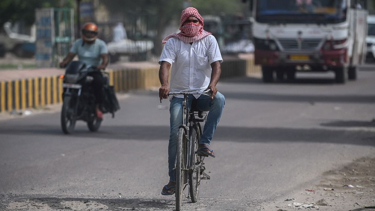 A cyclist covers his face with a cloth to shield from the scorching sun as he peddles along a road on a hot summer afternoon in Sri Ganganagar. Credit: AFP Photo