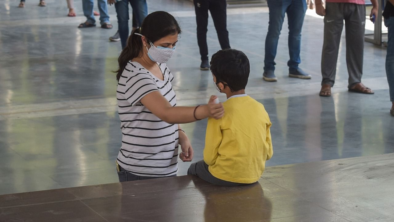 A mother reassures her child as she prepares to join a queue of people to receive first dose of Covid-19 vaccine, at a vaccination centre. Credit: PTI File Photo