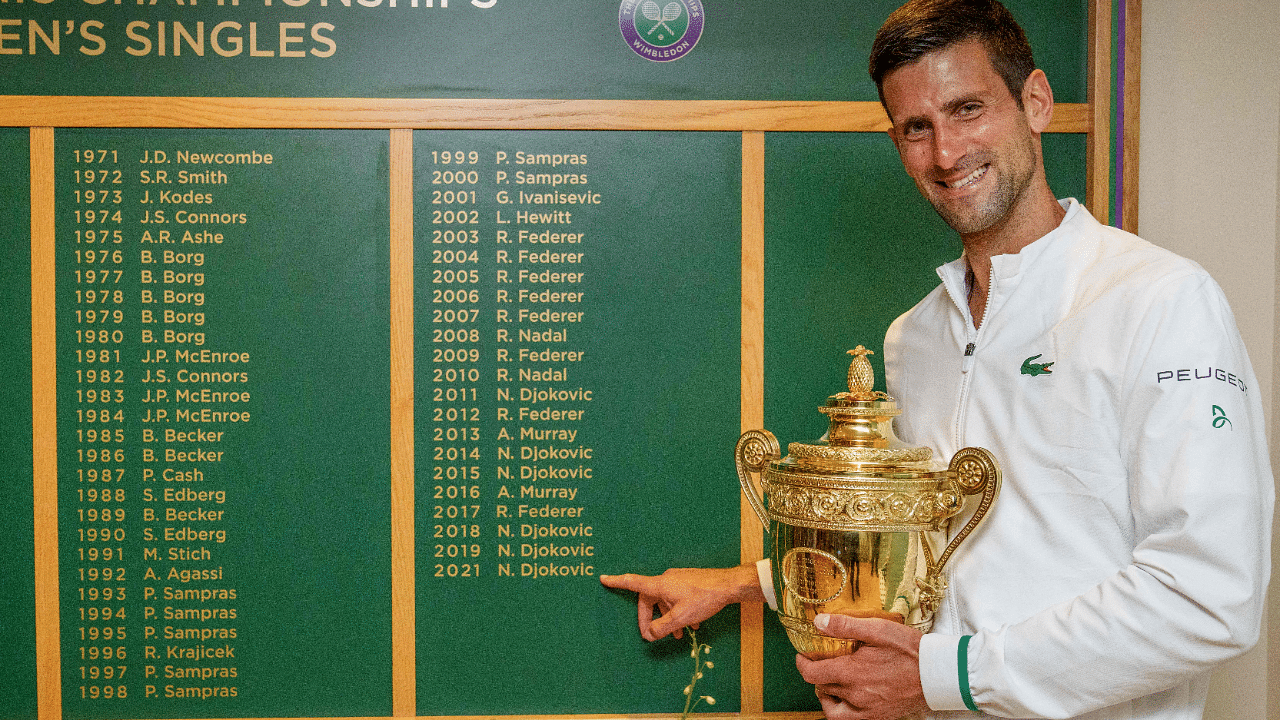 Serbia's Novak Djokovic holds the winner's trophy in front of the honours board and points to his name. Credit: AFP Photo