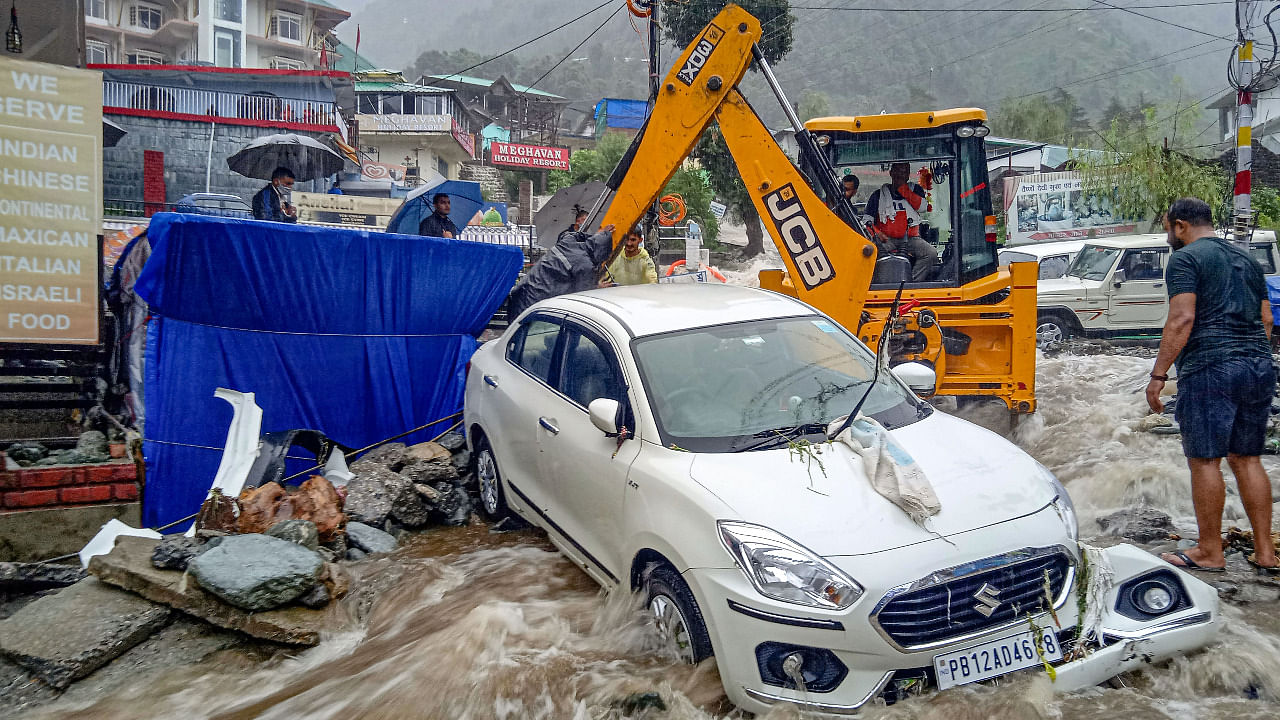 An earthmover machine removes a vehicle stuck in flood water near Bhagsunag, as heavy rains lashed the area after a cloudburst in McLeodganj near Dharamshala. Credit: PTI Photo