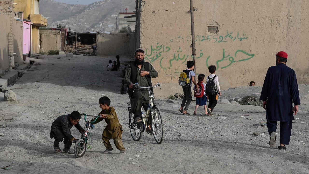 People pass by as children play with a cycle along a Kabul road. Credit: AFP Photo