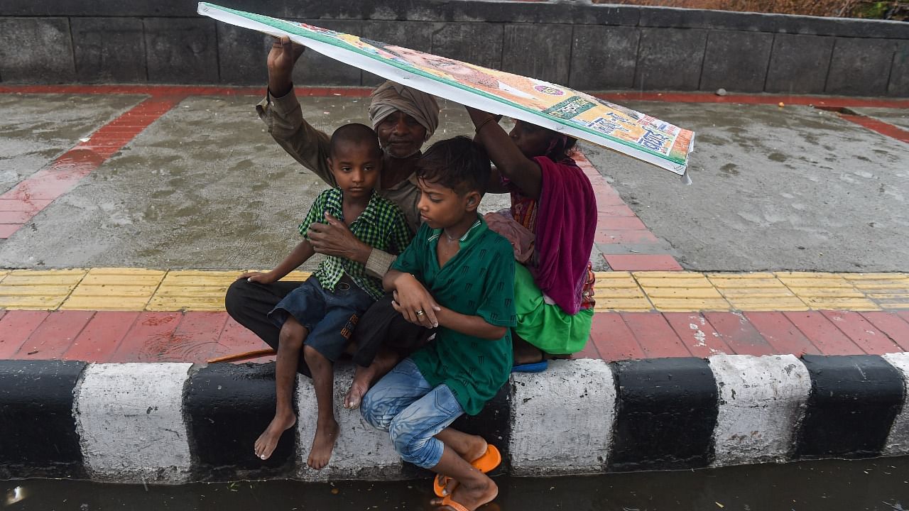 A family covers themselves under a hoarding during rain as monsoon reaches New Delhi, Tuesday, July 13, 2021. Credit: PTI Photo
