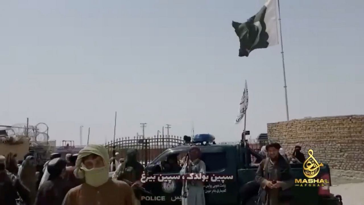 People stand in front of a vehicle as an Islamic Emirate of Afghanistan and a Pakistan's flag flutter in front of the friendship gate of Afghanistan and Pakistan at the Wesh-Chaman border crossing. Credit: Taliban Handout via Reuters