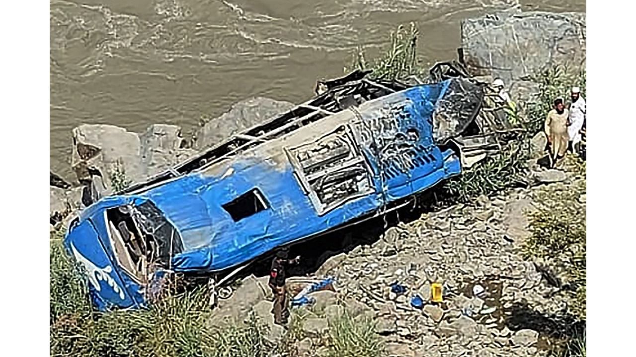 People stand next to a wreck after a bus plunged into a ravine following a bomb attack, which killed 12 people including 9 Chinese workers, in Kohistan district of Khyber Pakhtunkhwa province on July 14, 2021. Credit: AFP Photo