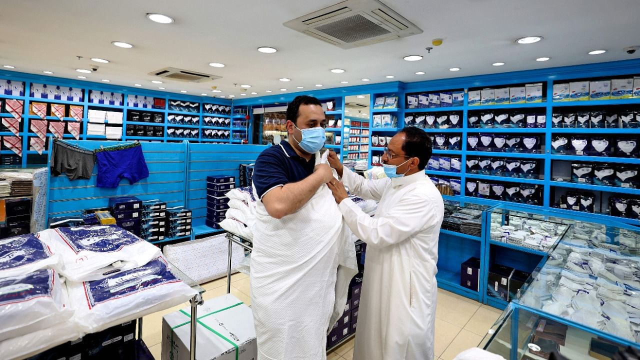 Egyptian Mohammed Alatar (L), 31, tries on Ihram, a simple garment representing a state of holiness worn by pilgrims performing the Hajj, at a local store in Saudi Arabia's capital Riyadh, on July 10, 2021, after he won a place to perform the yearly pilgrimage for the 2021 season. Credit: AFP Photo