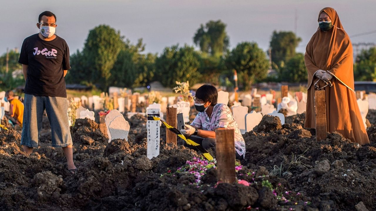 A family pray for their relative next to the grave at the burial site for the Covid-19 coronavirus victims at Keputih cemetery in Surabaya, East Java on July 17, 2021. Credit: AFP Photo