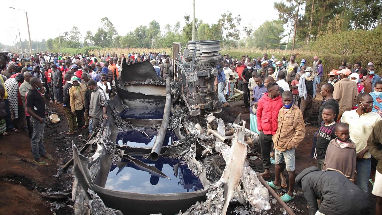 People stand next to a burnt out petrol tanker that burst into flames when it overturned in western Kenya, while a crowd thronged to collect the spilling fuel. Credit: AFP Photo