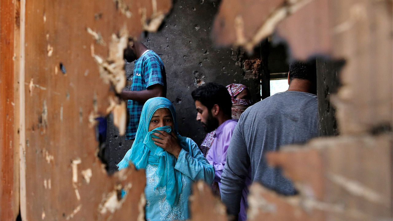 People are seen through a broken door of a residential house that, according to local media reports, was damaged during a gun battle between suspected militants and Indian security forces in Srinagar. Credit: Reuters Photo